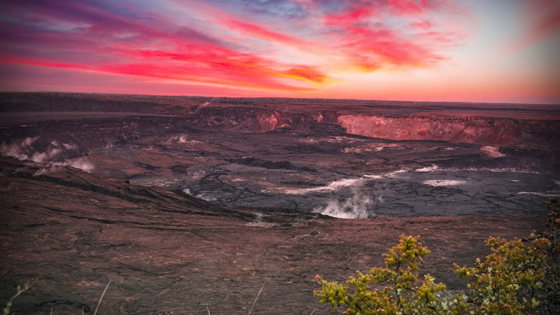 Volcanic crater with steam under vibrant sunset sky.